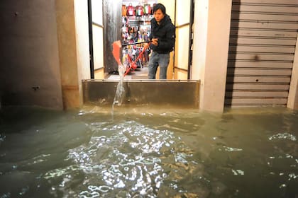 Un hombre saca el agua de un comercio luego de que la compuerta no resistiera la inundación, ya que la altura superó el promedio habitual.