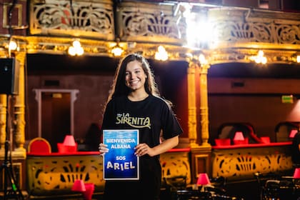 Albana Fuentes sonríe frente a cámara con una remera de La sirenita y un cartel que le da la bienvenida al papel que interpretará en el musical: la princesa Ariel