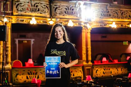 Albana Fuentes sonríe frente a la cámara con una remera de La sirenita y un cartel que le da la bienvenida al papel que interpretará en el musical: Ariel