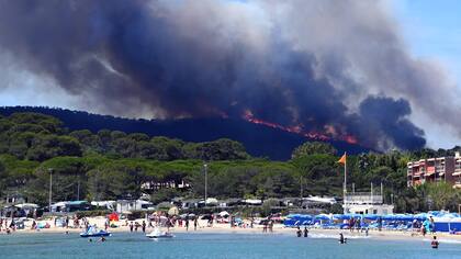 Algunas personas disfrutan de la playa mientras se incendia un bosque detrás de ellos en Bormes-les-Mimosas, sureste de Francia.