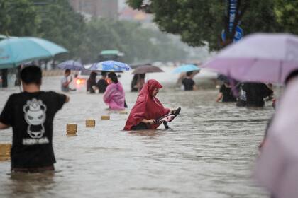 Algunas personas vadean las aguas de la inundación a lo largo de una calle después de las fuertes lluvias en Zhengzhou