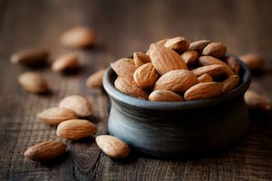 Almonds in a black bowl against dark rustic wooden background