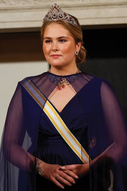Amalia con la tiara Pavo Real, una pieza con diamantes y rubíes creada para la reina Guillermina I por la casa Johann Eduard Schürmann & Co. El pelo recogido permite apreciar sus aros de rubíes y, a través de la capa transparente, el imponente collar.