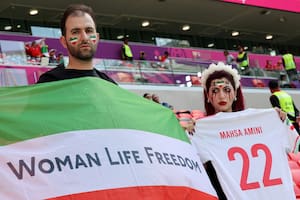An Iran's supporter with blood tears make up on her face holds a football jersey reading the name of Mahsa Amini, the 22-year-old Iranian Kurdish woman who died at the hospital after been arrested by the morality police for violating Iran's strict dress code, poses with another supporter holding a flag reading "Woman life freedom" as they attend the Qatar 2022 World Cup Group B football match between Wales and Iran at the Ahmad Bin Ali Stadium in Al-Rayyan, west of Doha on November 25, 2022. - Iran has been rocked by more than seven weeks of nationwide protests over the death of 22-year-old Kurdish Iranian woman Masha Amini while in the custody of the Tehran morality police. (Photo by Giuseppe CACACE / AFP)