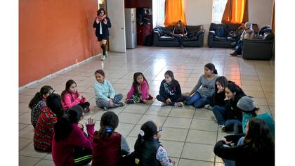 Angela, llegando, arriba y Selenna, sentadas en el círculo en la parte superior izquierda y vistiendo un buzo azul, toman una clase de teatro y danza con chicas en su centro comunitario Santiago de Chile.