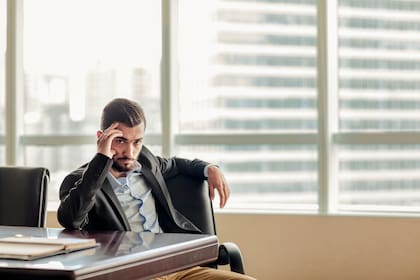 Annoyed businessman looking at computer monitor and talking on mobile phone. Frustrated male business professional talking on the phone while sitting at his work desk.