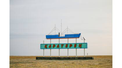 Un cartel con un barco y el nombre de un pueblo durante el atardecer fuera de la aldea de Karateren, cerca del mar de Aral, al sudoeste de Kazakhstan