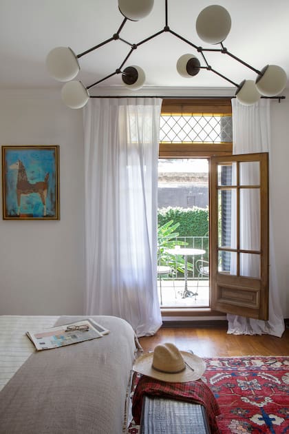 Araña de ocho luces opalinas (Dimm Iluminación), funda de edredón en tussor (Camba Home) y, al pie de la cama, banqueta de madera quemada.