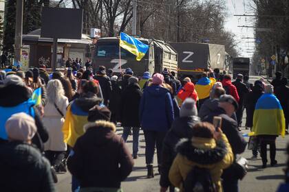 ARCHIVO - Personas con banderas ucranianas caminan hacia los camiones militares rusos durante una marcha contra la ocupación de Rusia, en Jersón, Ucrania, el domingo 20 de marzo de 2022. (AP Foto, archivo)