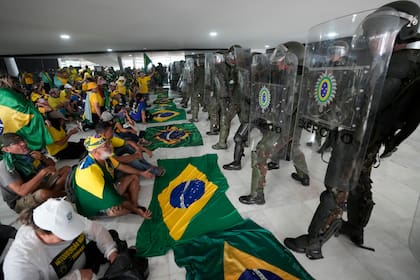 ARCHIVO - Simpatizantes del expresidente brasileño Jair Bolsonaro permanecen sentados frente a una hilera de policías militares dentro del Palacio de Planalto, luego de que se metieron al sitio oficial de trabajo del presidente, el domingo 8 de enero de 2023, en Brasilia, Brasil. (AP Foto/Eraldo Peres, archivo)