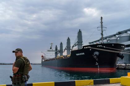 ARCHIVO - Un elemento de seguridad vigila el barco Navi-Star que permanece varado y lleno de granos desde la invasión de Rusia a Ucrania mientras aguarda la autorización para zarpar del puerto de Odesa, en Ucrania, el 29 de julio de 2022. (AP Foto/David Goldman)