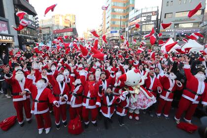 Voluntarios lanzan sus sombreros al aire mientras se reúnen para entregar regalos para los más vulnerables en el centro de Seúl, Corea del Sur