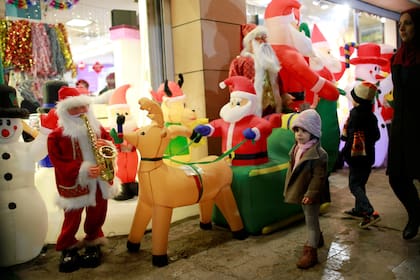 Los niños iraquíes caminan junto a una tienda que vende adornos navideños en Bagdad, Irak