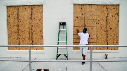 Un hombre instala tablones en las ventanas de una tienda de antiguedades en Florida, Estados