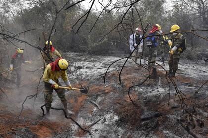 Un grupo de bomberos remueve la tierra para eliminar restos de brasas que puedan generar nuevos incendios
