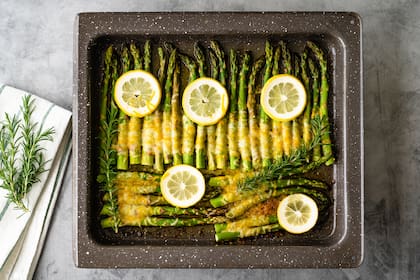 Asparagus baked with sliced lemon, fresh rosemary, butter, and cheese. Fresh baked delicious meal close up on kitchen table, flat lay
