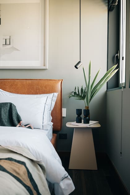 Aunque de lejos parece formar un continuo con la base de la cama, el respaldo en cuero (Larralde-Spelzini) con reborde pespunteado está amurado. Lámparas colgantes ‘L40′ (San Isidro Luz).