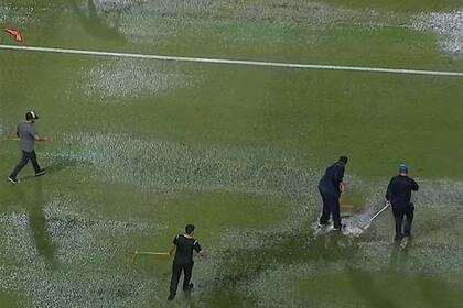 Auxiliares de Independiente intenta quitar el agua del campo de juego.