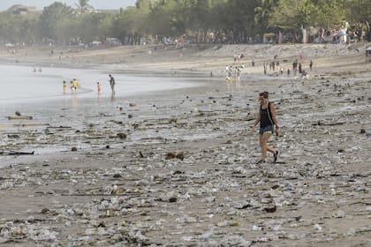 Turistas y locales caminan entre basura en la orilla de la playa de Kuta en Bali, Indonesia