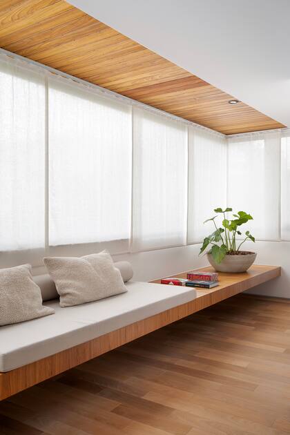 Banco flotante con colchoneta a medida, almohadones, cortinas corredizas en tramos y verde interior: el rincón perfecto para disfrutar de un libro.
