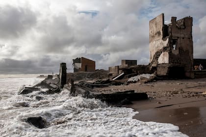 Mujeres pasan junto a los edificios destruidos a lo largo de la costa erosionada de Bargny