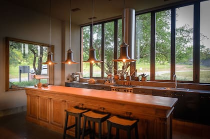 Barra de madera y colgantes galponeras hechas a medida, igual que la campana tubular. Mesada en 'Dekton' (Marmolería La fontana) y amoblamiento revestido en chapa metálica