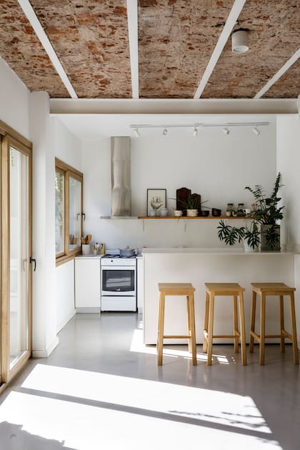 Barra de melamina ‘Lino’ (Faplac) con mesada ‘Blanco Nube’ (Purastone), diseñada por el Estudio. Banquetas (Cousy Home). Riel de spots (Griscan). Extractor (TST). En el estante de petiribí macizo, macetas (Planta Somos), tablas (Vienede), objetos de cerámica (Antes Pella).