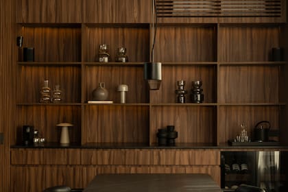 Biblioteca de melamina nogal (Faplac) hecha por Módulo Quatro y mesada de granito negro con terminación leather hecha a medida (Estudio JDD). El mueble contiene también una cava y, arriba, oculta los equipos acondicionadores.
