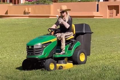 Bien protegida del sol, ella misma se ocupa del cortar el pasto subida en un tractor John Deere.