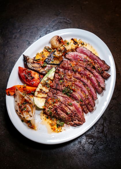 Bife ancho asado lentamente a la parrilla "al punto perfecto" con chimichurri y vegetales ahumados, uno de los más pedidos de la casa