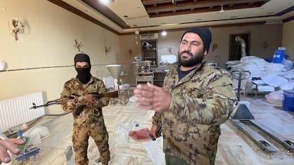 Bilal, el miliciano que controla la fábrica, de pie con su kalashnikov al hombro, vestido con camuflaje y un gorro negro, vigilando desde la entrada de la mansión.