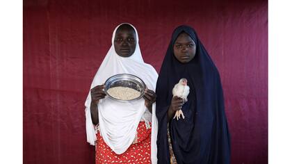 Binta Lawal sostiene un tazón de comida de aves de corral con Aisha Buba