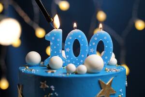 Birthday cake number 100 stars sky and moon concept, blue candle is fire by lighter. Copyspace on right side of screen. Close-up view