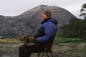 Bob Kull sentado en un silla con su gato en el regazo en la Patagonia chilena