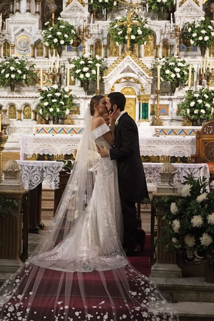 El beso, de película, emocionó a todos. La novia llevó un traje de Gabriel Lage, con escote off shoulder y cola capilla, realizado en tul de seda bordado íntegramente a mano. Angie completó el look con un gran velo y un ramo de orquídeas.