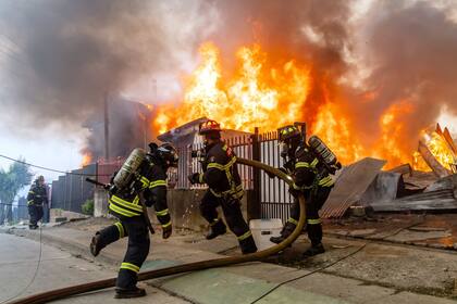 Bomberos combaten un incendio en una casa mientras los incendios forestales arden en Lirquen, Chile, el domingo 18 de enero de 2026.