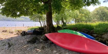Botes y kayaks a pie de un frondoso árbol en la playa del poblado escocés de Lawer