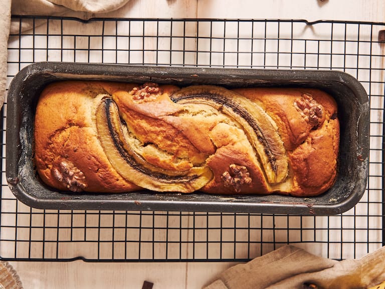Vertical shot of delicious banana bread in a loaf pan with chocolate chunks and walnut on a table