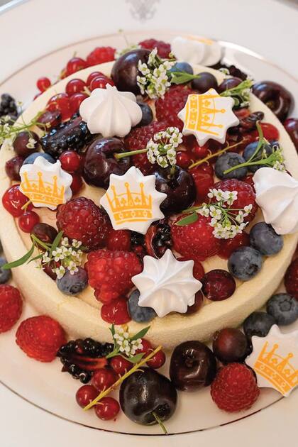 Cada mesa tenía una torta de cumpleaños rellena de mermelada de fresa, cubierta con mousse de vainilla y chocolate blanco y decorada con frutos rojos y una corona impresa sobre los merengues.