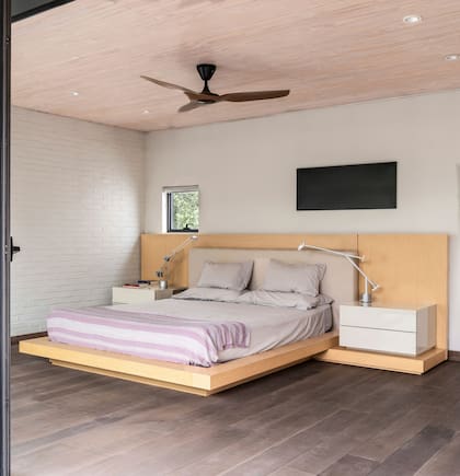 Cama tipo tatami con mesas de luz laqueadas y respaldo forrado en lino.