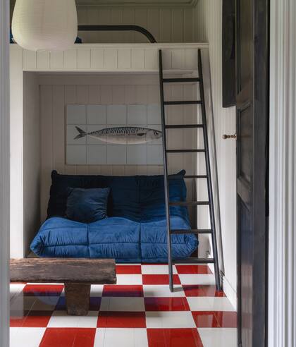 “Cambiamos el solado por madera vitrificada, que hace que los ambientes brillen y luzcan más grandes. Los pinté todos a mano: para estos cuadrados, ni siquiera usé cinta, solo lápiz y regla”. Sobre el sofá azul de Ligne Roset, rompecabezas con pez. La cama, subiendo la escalera.