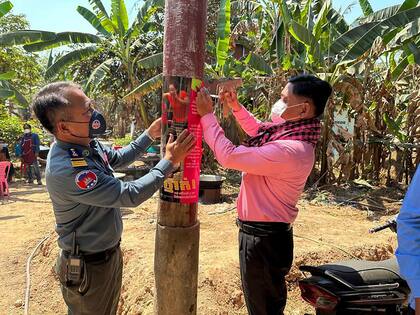 En esta foto publicada por el Ministerio de Salud de Camboya, un oficial de salud animal de Camboya, a la derecha, y un oficial de la policía militar colocan carteles sobre la concientización sobre las amenazas del virus H5N1 con la esperanza de educar a los aldeanos para que cuiden su salud, en la provincia oriental de Prey Veng, Camboya