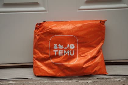 Canadá, 20 de julio de 2023: Paquete de bolsa rectangular naranja Temu con logotipo, entregado apoyado contra una puerta blanca