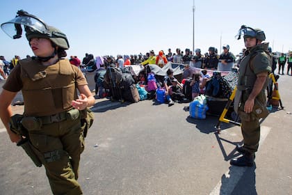Carabineros al lado de migrantes sentados en una carretera cerca de Arica, Chile, el jueves 27 de abril de 2023.