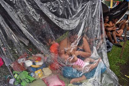 Una mujer amamanta a su bebé bajo un plástico para protegerse de la lluvia