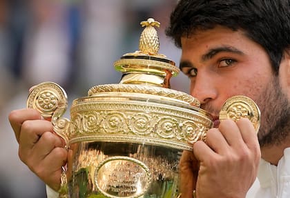 Carlos Alcaraz besando el prestigioso trofeo de Wimbledon, al imponerse en 2024, ante Novak Djokovic; también se coronó en el All England en 2023