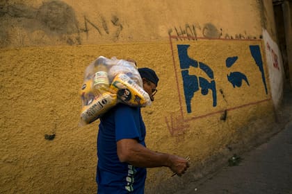 Carlos Gonzales lleva una bolsa con comida entregada por el gobierno para las personas más pobres en frente de un mural que muestra los ojos del fallecido presidente de Veneuzela, Hugo Chávez, en el barrio de Antimano en Caracas, Venezuela, el 29 de enero