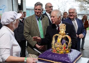 Carlos III saluda a una empleada al recibir una torta en forma de corona durante su visita a Berlín