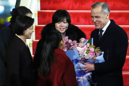 Carney recibe un ramo de flores de Lu You Ci, de 11 años, en su ceremonia de bienvenida tras aterrizar en Pekín