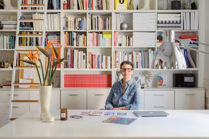 Carolina Aubele sentada en su escritorio delante de la biblioteca diseñada a medida. Botas de gres (Artefactos).